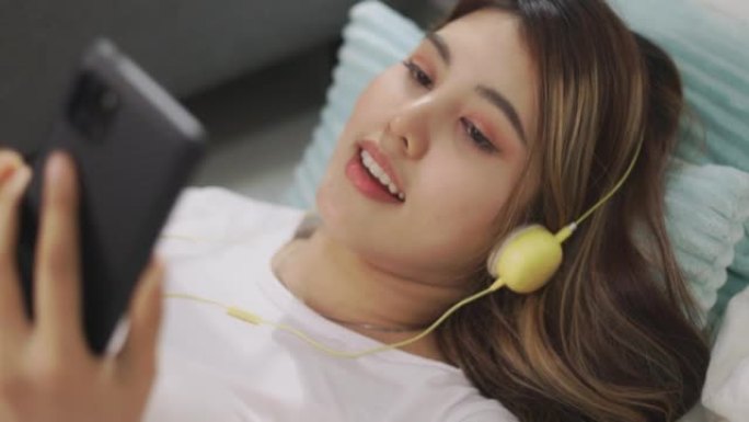特写快乐的亚洲女人戴着耳机听音乐，独自在家享受慵懒的周末爱好时光。