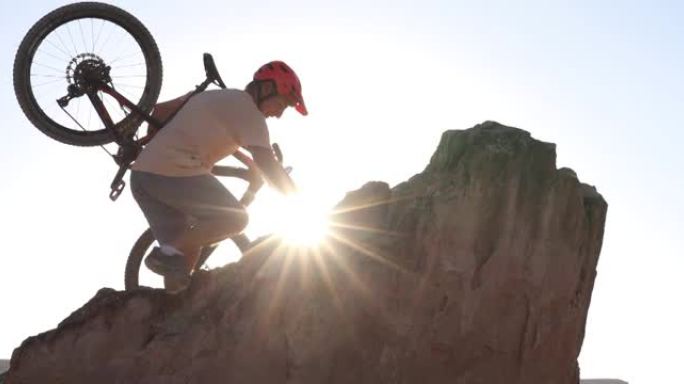男性山地自行车手攀登沙漠地面上方的岩石山脊