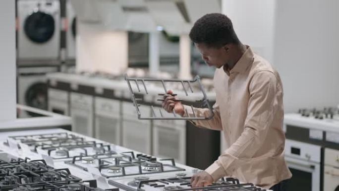 年轻的非洲裔美国人在家电商店选择炉灶，看烹饪表面，单身男人在购物