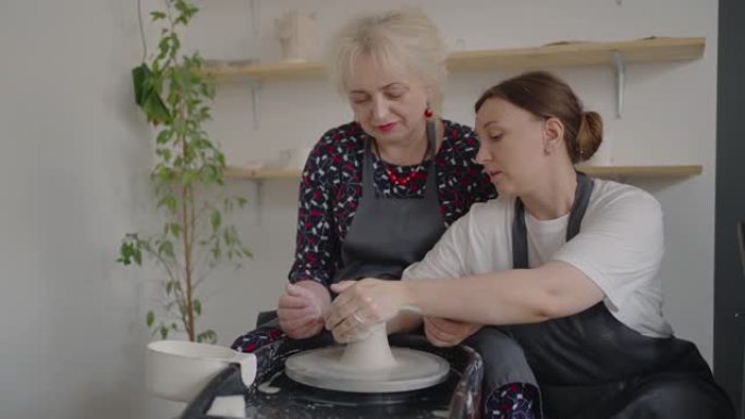 一位女大师在为老年人上课的同时分享自己的技能。向祖母展示用陶瓷粘土在陶工轮上工作的技术