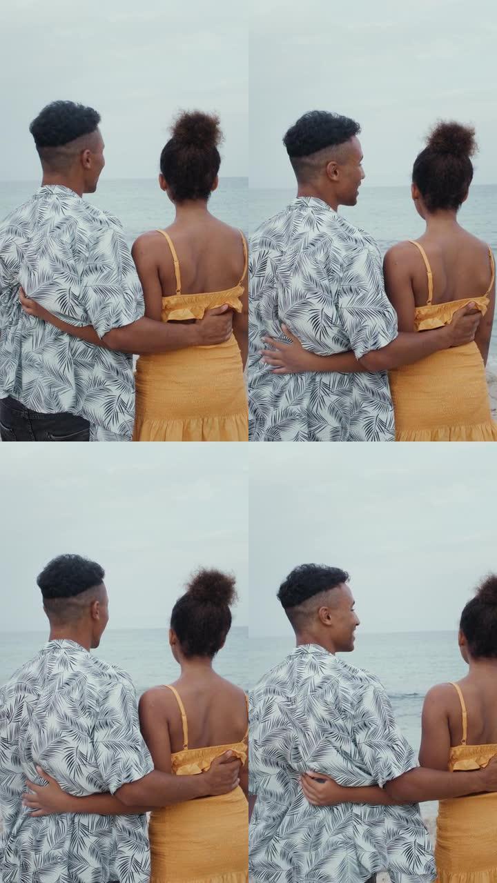 相爱的非洲族裔夫妇互相抱着。海滩上的浪漫漫步垂直视频