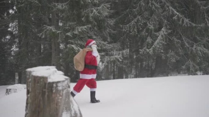 打扮成圣诞老人的男人走在白雪皑皑的森林中，肩上挂着一袋礼物