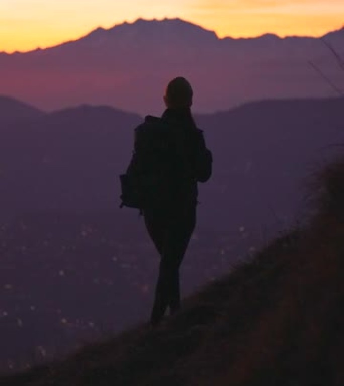 女性徒步旅行站在山顶上，享受新鲜空气，欣赏下面的湖泊、日落和城市