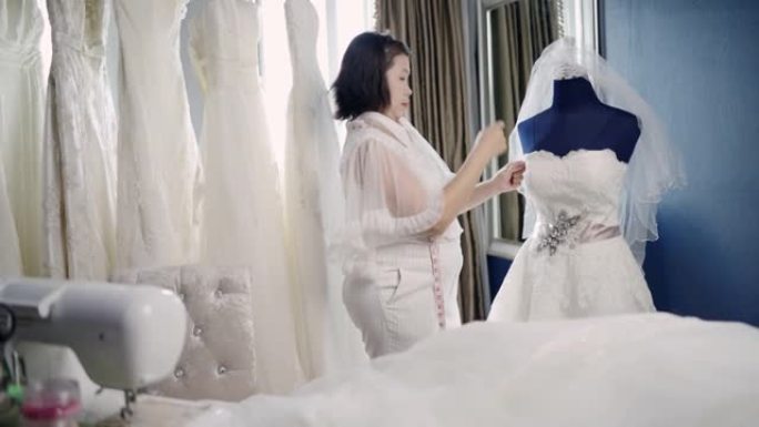 亚洲女裁缝在身体周围剪裁新娘的礼服。