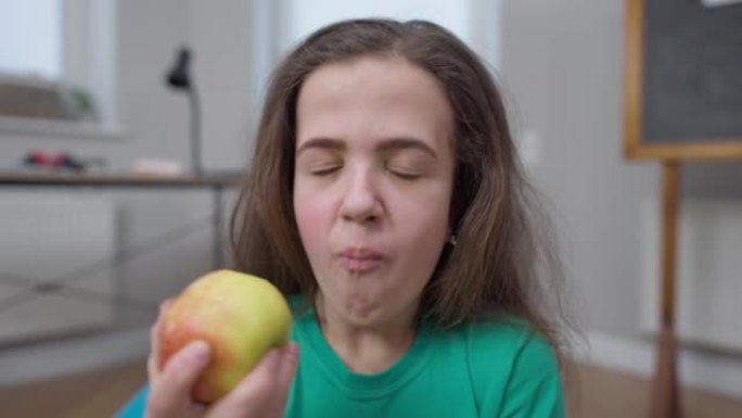 小人咬健康的维生素苹果微笑着看着相机咀嚼水果。快乐美丽的高加索黑发女人在室内享受健康食物的特写肖像。