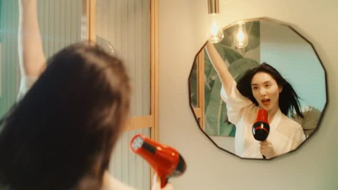 感觉棒极了。亚洲族裔妇女享受早上的浴室活动，在镜子前玩得开心。干燥头发和跳舞