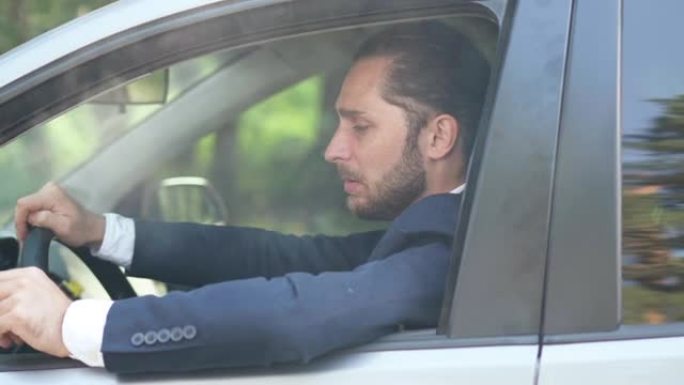 侧视年轻体贴的男子坐在汽车驾驶座上吸烟。穿着西装和香烟在户外的高加索人的肖像。坏习惯和成瘾概念。