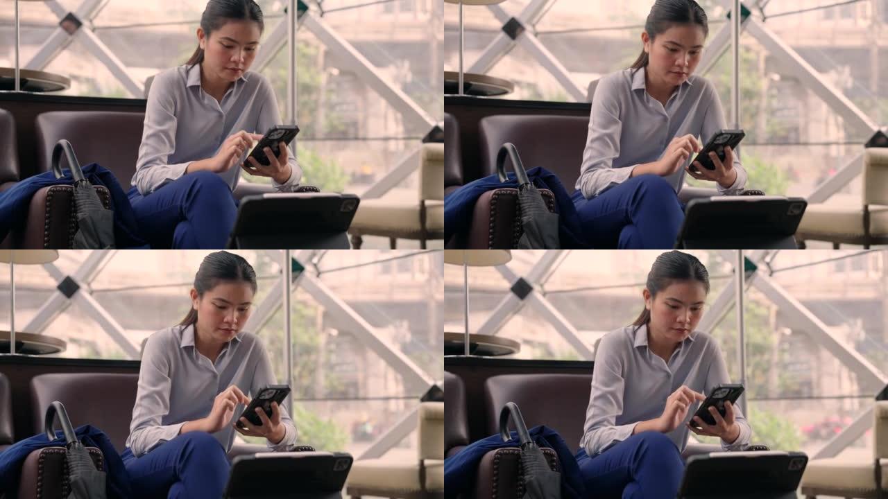 坐在咖啡馆里的亚洲女人。她在咖啡店内使用手机和平板电脑在现场工作。