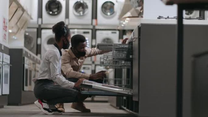 两个戴着口罩的人在新型冠状病毒肺炎大流行的五金店购物，黑人配偶正在选择洗碗机