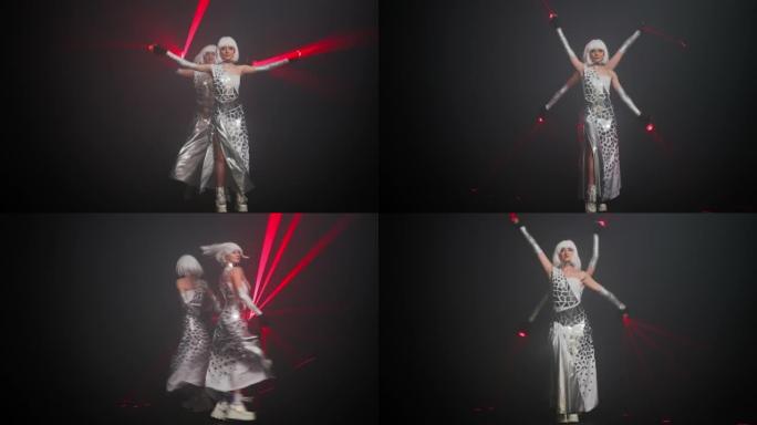 专业女舞者戴着红色激光束在舞台上表演。两名穿着未来派服装的白人妇女看着相机跳舞，跳舞当代艺术舞蹈。