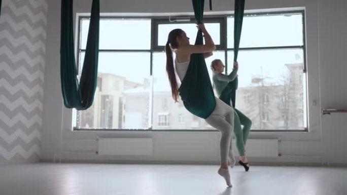 两个女人的内部拍摄在瑜伽馆用吊床练习不同的反向反重力瑜伽。精神与身体，两个人的努力与成就观念之间的平