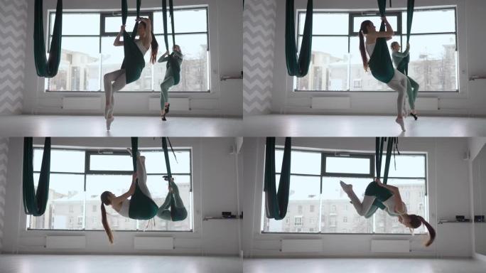 两个女人的内部拍摄在瑜伽馆用吊床练习不同的反向反重力瑜伽。精神与身体，两个人的努力与成就观念之间的平