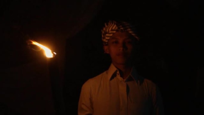 一名穆斯林男子在漆黑的夜晚孤独地站着，手持竹火把
