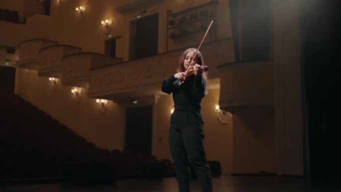 年轻的女小提琴演奏者的肖像在音乐厅演奏小提琴，歌剧院的女小提琴手