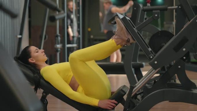 西班牙裔妇女在健身俱乐部使用印刷机。年轻女子穿着黄色运动服在模拟器中锻炼脚，