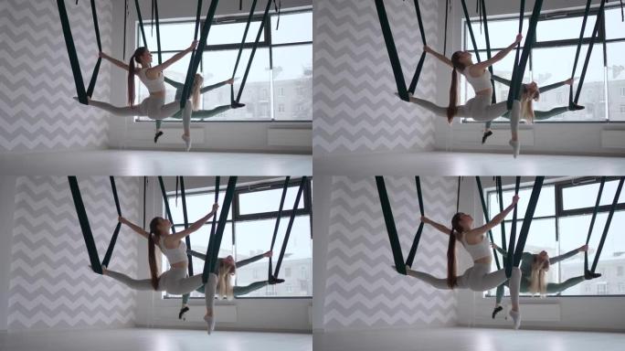 两个女人在空中吊床上表演麻线。空中健身房里的妊娠纹。航空瑜伽