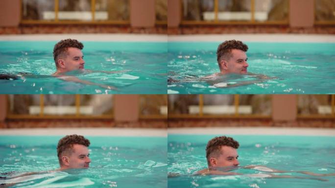 年轻的白人男子正在现代温泉中心的室外游泳池游泳，放松和娱乐