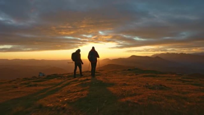 空中两名男性徒步旅行者在日落时在山顶上行走