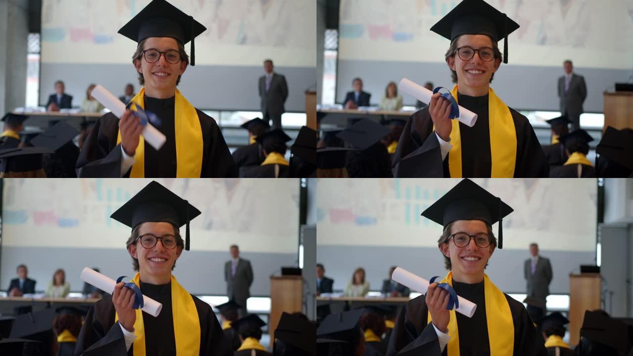 英俊的年轻男学生在毕业典礼上拿着hid文凭，面对镜头微笑