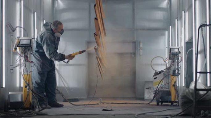 一名身穿防护服和口罩的男子通过喷枪以慢动作将油漆喷洒在钢制零件上。