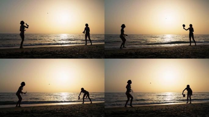 日落时在海滩上享受桨网球的两个女人的剪影