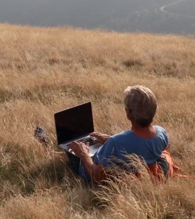 男子在山区草草草地上使用笔记本电脑
