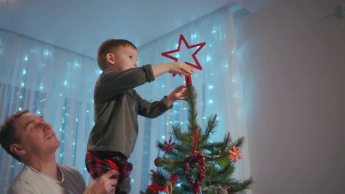 爸爸把男孩举到圣诞树的顶部，在顶部放一颗圣诞星。父子一起装饰圣诞树