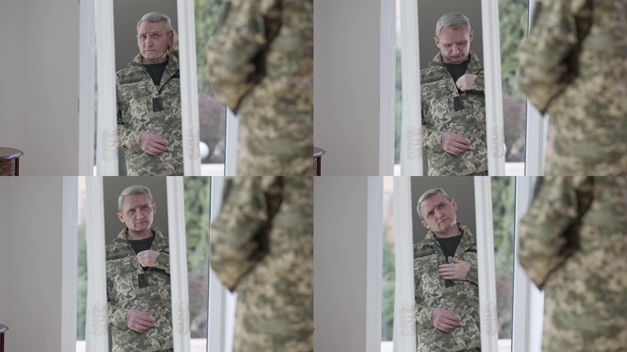 中景，一个严肃的军人站在家里的镜子里。自信英俊的中年白人士兵准备服兵役的肖像。生活方式和信心。