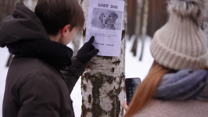 关于树上迷路的狗的公告，青少年朋友在冬季户外拨打电话号码。在模糊的高加索男孩和女孩的肩膀上射击，帮助