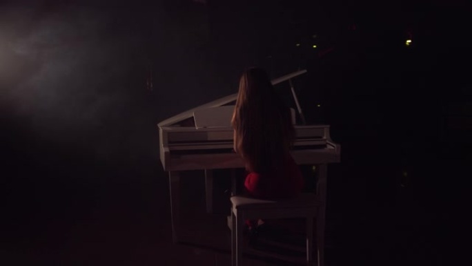 4k女钢琴家的镜头在音乐会舞台上演奏美丽的三角钢琴。一个女人在音乐厅弹钢琴。舞台灯光和背景上的轻雾