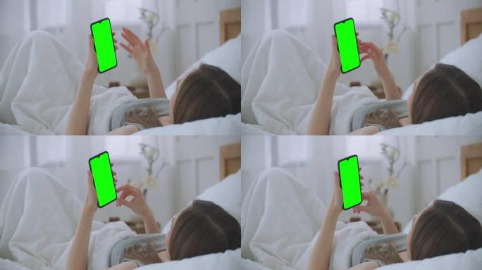 美丽的女人使用智能手机，在灯光室显示触摸屏。年轻迷人的黑发女人早上在卧室和朋友通过智能手机网络摄像头