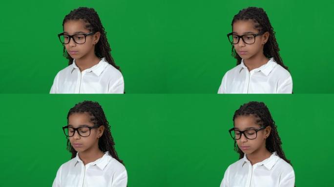 心烦意乱的书呆子非裔美国少女在绿屏上低头。在chromakey背景下戴眼镜的悲伤沮丧绝望的受歧视少年