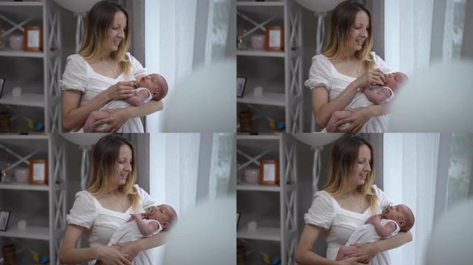 微笑的女人站在客厅的窗户上，将奶嘴放在初生婴儿的嘴里，慢动作摇晃着儿子。快乐的高加索母亲在家里照顾婴