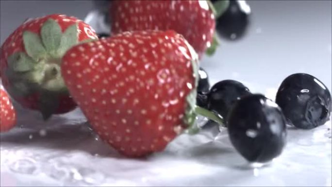 蓝莓和草莓在白色背景上滚动。慢动作