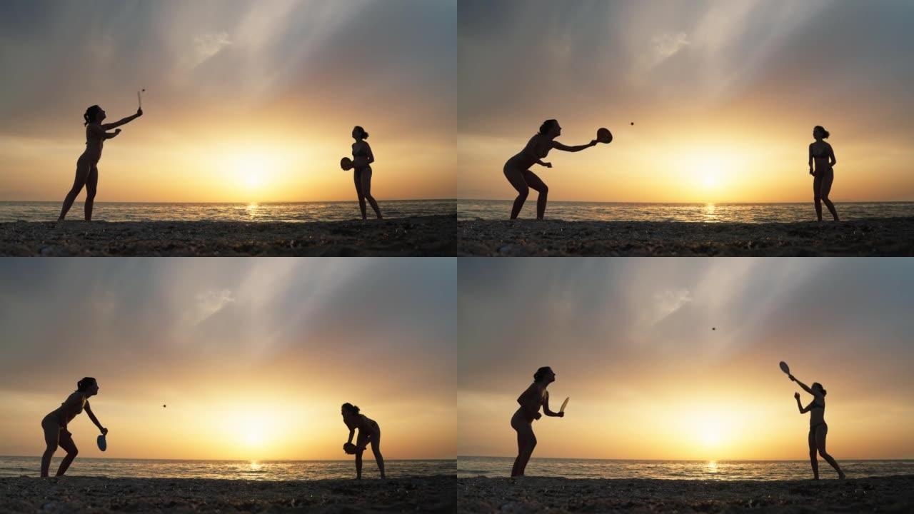 日落时在海滩上享受桨网球的两个女人的剪影