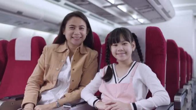 微笑的母亲坐在飞行中的女儿旁边