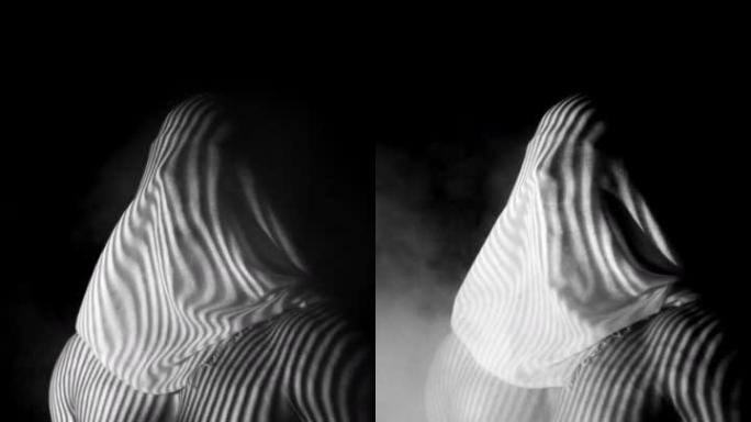 灰色肌肉男子与面纱的脸摆姿势的相机与抽象的照明效果与黑色背景的烟雾效果。垂直视频