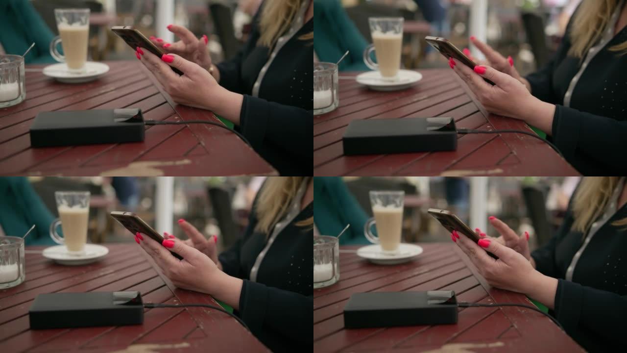 一名咖啡馆游客坐在街头咖啡馆时，用外部电池给手机充电。