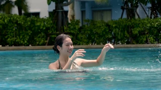 4k，一位可爱的亚洲少女女性游客在游览和在酒店放松的一天中，在游泳池里快乐地游泳。在晴朗的日子里，一