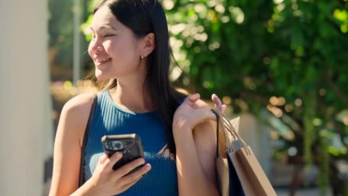 亚洲女人在户外购物中心购物后走路和微笑的购物袋。