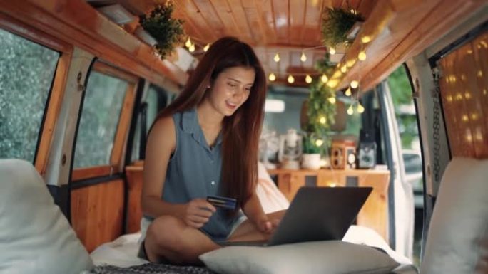 年轻女子在度假旅行时使用笔记本电脑和信用卡