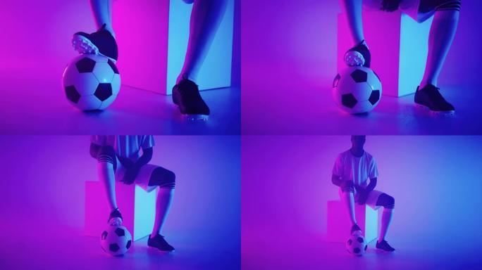 在演播室蓝红色霓虹灯下慢动作站立在球上的一名职业黑人足球运动员的脚的特写镜头。巴西足球运动员脚踩球摆