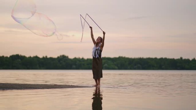 一位年轻的女孩艺术家使用巨大的肥皂泡展示魔术。在日落时使用棍棒和绳索创建肥皂泡，以展示戏剧马戏团表演