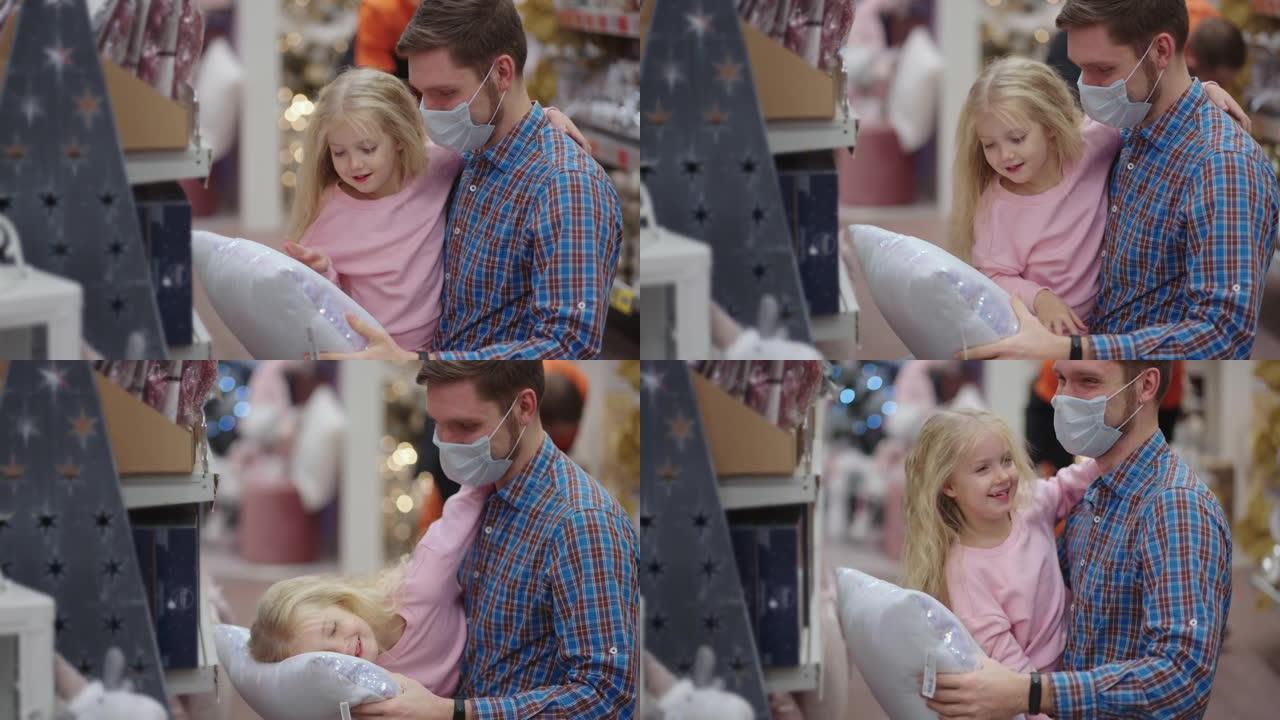 选择一个漂亮的枕头。一位父亲戴着医用口罩，带着女儿在圣诞节前夕选择珠宝和玩具来装饰房屋和圣诞树