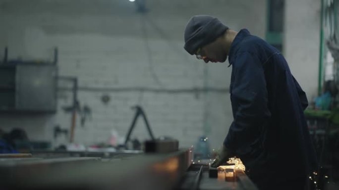 这个人在一家工厂工作。一名戴着防护眼镜的人从事金属研磨抛光和剥离钢金属结构的工作。