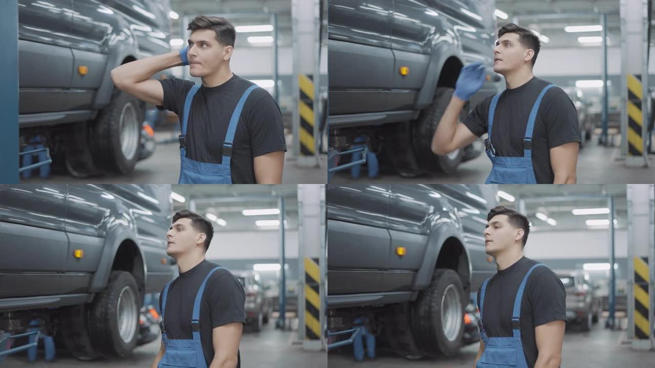 不确定年轻的高加索修理工在汽车车间里挠头看着破损的汽车。不确定的黑发英俊的服务人员在汽车修理厂检查车