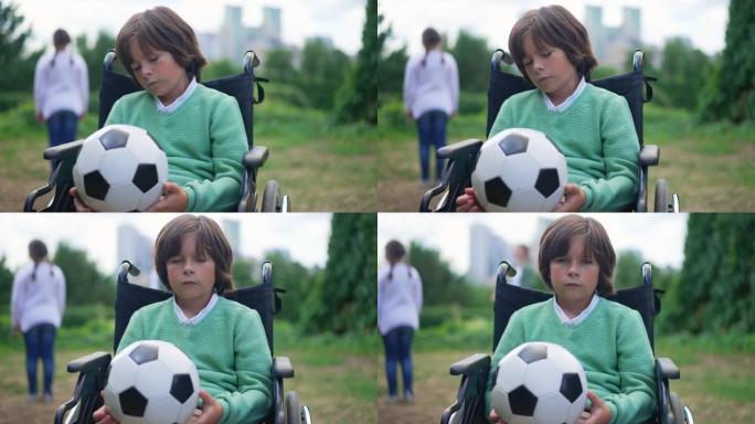 中枪悲伤的高加索男孩，坐在轮椅上思考着球，看着慢动作的相机。不幸的沮丧孩子的肖像在户外夏季公园摆姿势