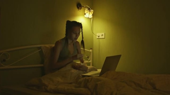 A young woman is lying in bed eating popcorn and e