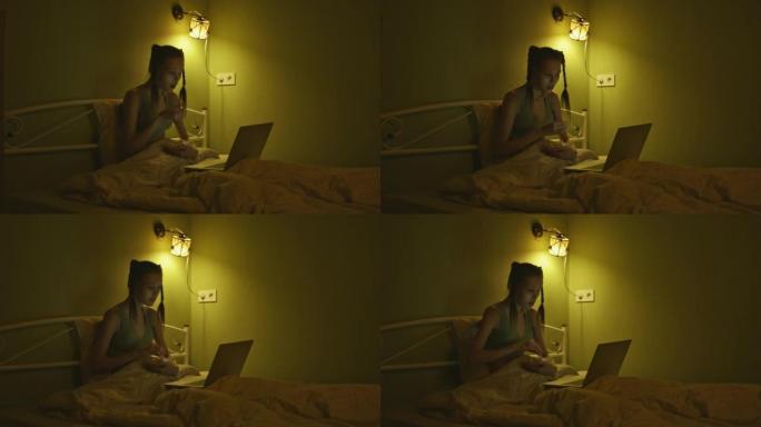 A young woman is lying in bed eating popcorn and e