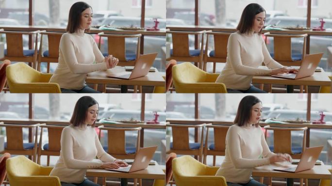 在咖啡馆里坐在桌子上用笔记本电脑上网的体贴女人的侧视图。自信的白人千禧一代分析初创公司午餐休息在餐厅